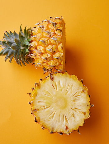 Fresh pineapple halved, showcasing its vibrant interior, on a yellow background. HD phone wallpaper