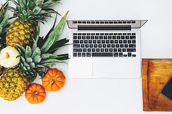 Stylish workspace featuring a laptop, pineapples, and pumpkins on a white background. HD wallpaper