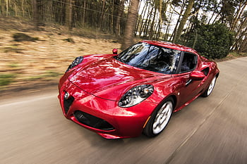 A sleek red sports car driving fast on a forest road, showcasing speed and luxury. HD wallpaper