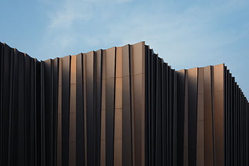 Sleek modern building facade with unique design set against a clear blue sky. HD wallpaper