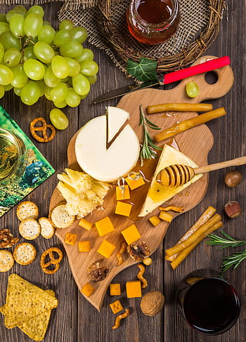 A delicious assortment of cheeses, crackers, and grapes on a wooden board for a gourmet appetizer. HD phone wallpaper