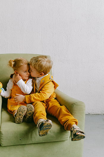Two young siblings embracing lovingly on a cozy green armchair indoors. HD phone wallpaper
