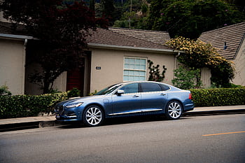 A sleek blue luxury car parked in front of a suburban house with greenery. HD wallpaper