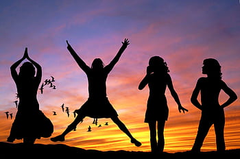 Silhouetted group of women joyfully jumping and posing against a vibrant sunset sky with birds flying. HD wallpaper