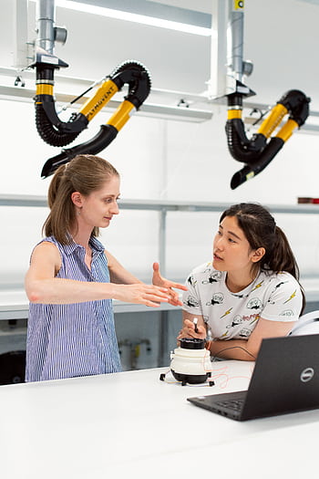 Two women engineers discussing a project in a high-tech lab environment. HD phone wallpaper