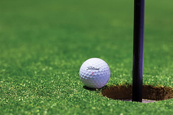 Close-up of a golf ball near a hole on a vibrant golf green, capturing the moment of near success. HD wallpaper