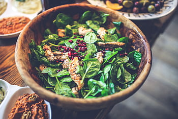 A delicious and vibrant spinach salad with grilled chicken and pomegranate seeds in a wooden bowl. HD wallpaper