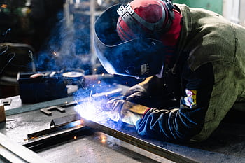 A welder works on metal fabrication indoors, creating bright sparks and smoke. HD wallpaper