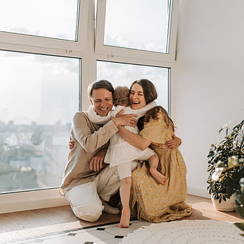 A joyful family hugging tightly near a window, radiating warmth and togetherness. HD phone wallpaper