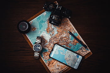 Top view of travel essentials including a map, camera, , watch, and lens on a wooden surface. HD wallpaper