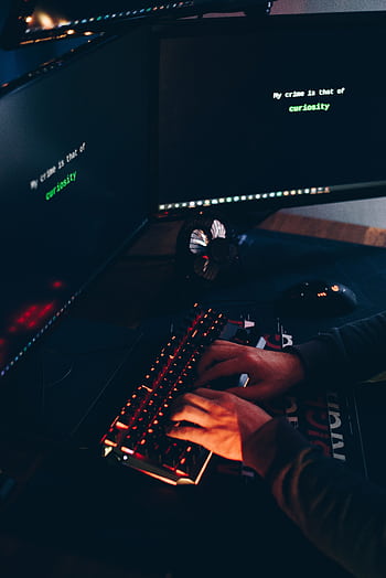A person typing on a keyboard in a dark room with screens displaying text. HD phone wallpaper