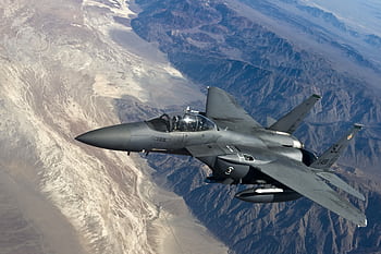 A military fighter jet flying above rugged mountain ranges, showcasing advanced aviation technology. HD wallpaper