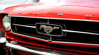 Close-up of a vintage red Ford Mustang's iconic front grille and logo. HD wallpaper