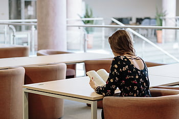 A woman sits comfortably indoors, reading a book in a modern library setting. HD wallpaper