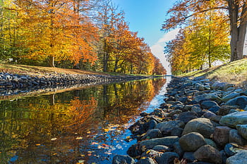 A scenic canal in Horten, Norway, with vibrant autumn foliage reflecting in the water. HD wallpaper