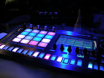 Close-up of an illuminated DJ mixer with vibrant LED pads in a dark studio environment. HD wallpaper