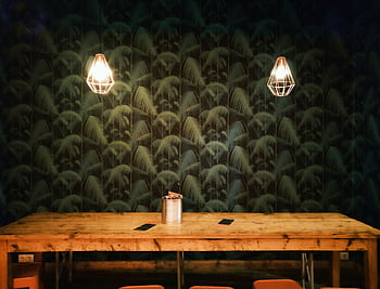 Cozy rustic interior featuring geometric pendant lamps and a large wooden table against a patterned wall. HD wallpaper