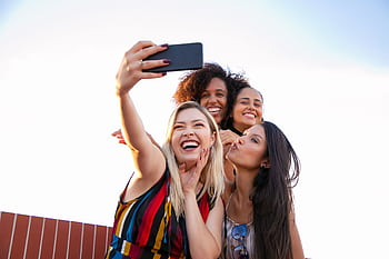 A joyful group of diverse women capturing a fun moment outdoors with a smart. HD wallpaper