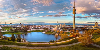 A captivating panoramic view of Munich's Olympic Park during sunset, showcasing the lake and iconic tower. HD wallpaper