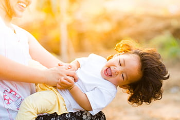 A joyful mother and child laughing together in a sunny outdoor setting, capturing family happiness. HD wallpaper