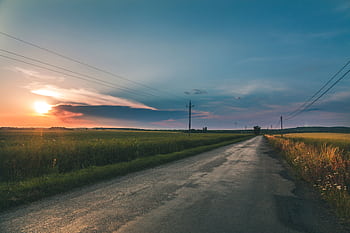 A serene rural road leading through lush fields under a colorful sunset sky. HD wallpaper