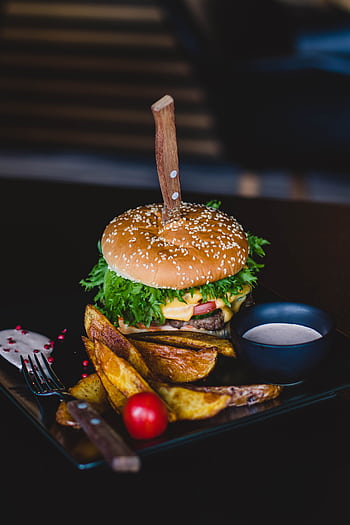 Close-up of a gourmet cheeseburger with wedges and tomato on a black plate. HD phone wallpaper