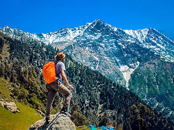 Man exploring breathtaking mountain scenery with snow-capped peaks under a clear blue sky. HD wallpaper