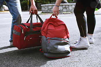 Two travelers holding red bags on a street, symbolizing travel and exploration. HD wallpaper