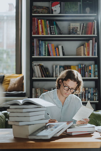 A young man focuses on studying amidst a bookstore environment, surrounded by books. HD phone wallpaper