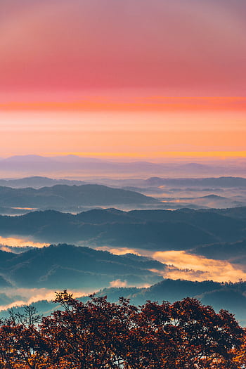 A breathtaking view of rolling mountains at sunset with fog and vibrant skies. HD phone wallpaper