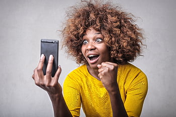 Joyful woman in yellow showing surprise and excitement at smart message indoors. HD wallpaper