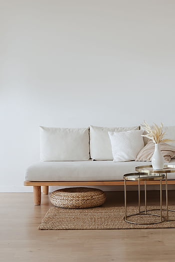 A chic minimalist living room featuring a white sofa with cushions, dried flowers in a vase, and a wooden floor. HD phone wallpaper