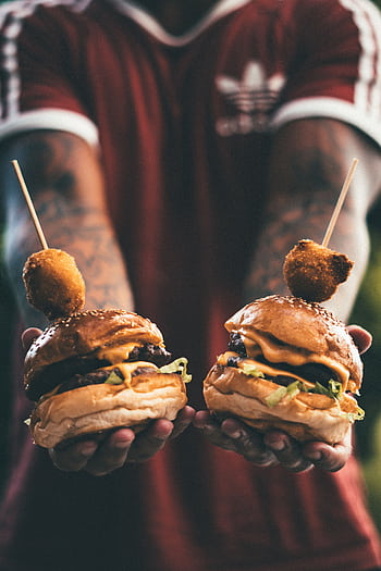 Two cheeseburgers held by a tattooed individual, showcasing juicy meat, cheese, and lettuce. HD phone wallpaper