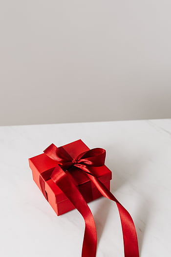 A red gift box with a satin bow on a marble surface, perfect for celebrations. HD phone wallpaper
