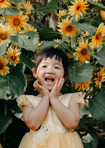 A young girl joyfully smiling amidst vibrant sunflowers on a sunny day. HD phone wallpaper