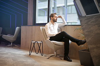 A thoughtful man in a modern office interior, sitting and looking outside. HD wallpaper