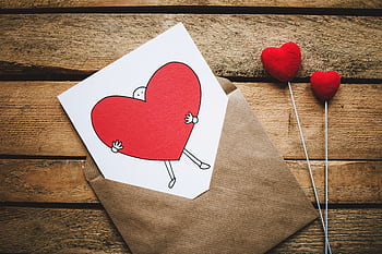 A love card with a red cartoon heart in an envelope on a rustic wooden table, perfect for Valentine's Day. HD wallpaper