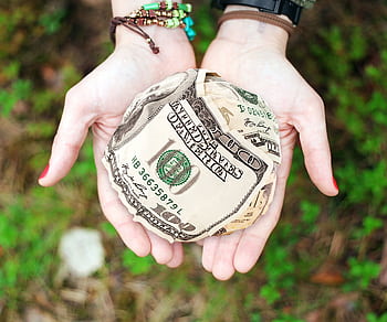 Hands holding crumpled money outdoors, symbolizing charity and financial support. HD wallpaper