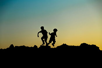 Silhouette of two children joyfully playing outdoors at sunset, capturing a moment of adventure. HD wallpaper