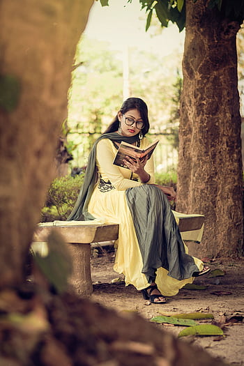 South Asian woman reading a book on a bench in a serene outdoor park setting. HD phone wallpaper
