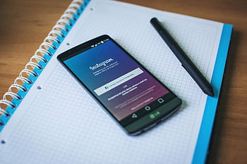 A smart displaying Instagram on a notepad with a pen, symbolizing social media and productivity. HD wallpaper