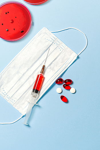 Face mask, syringe, and pills on a blue background, symbolizing healthcare and medical research. HD phone wallpaper