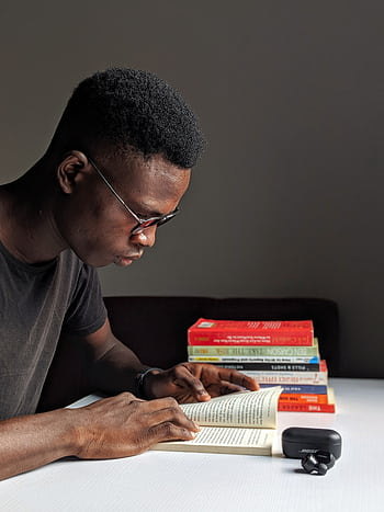 Young man studying intently with books in library setting. HD phone wallpaper