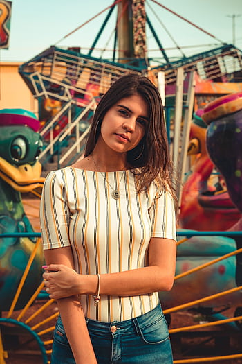 Young woman posing confidently at a vibrant amusement park. Perfect for fashion and lifestyle projects. HD phone wallpaper