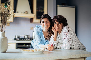 A mother and daughter bonding in the kitchen, smiling and enjoying their time together. HD wallpaper