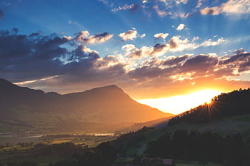 Dramatic sunset over Swiss mountains with vibrant colors and sun rays shining through clouds. HD wallpaper
