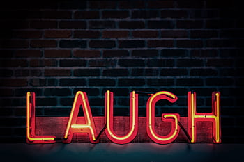Bright neon sign displaying 'LAUGH' against a dark brick wall, creating a vibrant mood. HD wallpaper