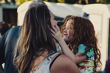 A heartwarming scene of mother and daughter embracing in a sunlit outdoor setting, symbolizing love and happiness. HD wallpaper
