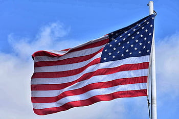 The American flag waving majestically against a vibrant blue sky, symbolizing patriotism and dom. HD wallpaper
