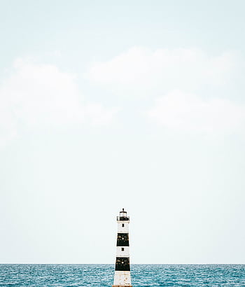 A solitary lighthouse stands against a clear sky and a calm ocean, showcasing minimalist serenity. HD phone wallpaper
